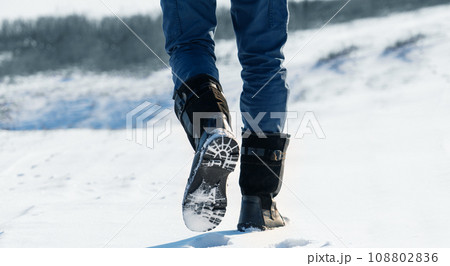 A traveler in boots walks along a snowy winter road 108802836