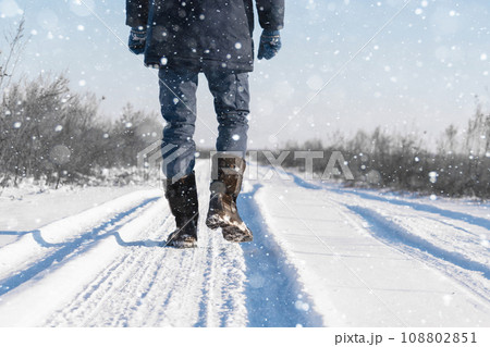 A traveler in boots walks along a snowy winter road 108802851