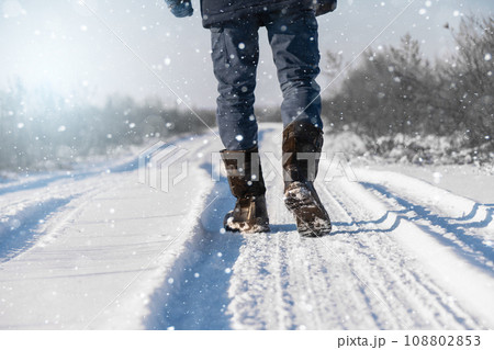 A traveler in boots walks along a snowy winter road 108802853
