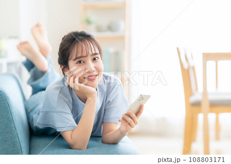 リビングのソファでスマホを見る若い女性 リビングのソファでスマホを見る若い女性 108803171
