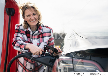 Woman in a plaid shirt charging an electric car Woman in a plaid shirt charging an electric car 108804769