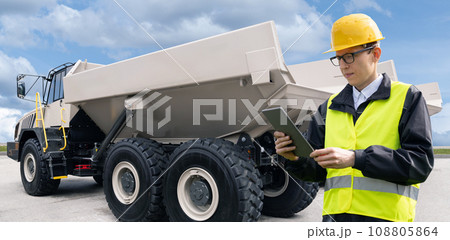 Engineer with tablet computer stands next to mining truck 108805864