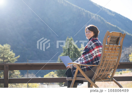 田舎のウッドデッキでリモートワークをする女性の秋冬 カメラ目線の広角 田舎のウッドデッキでリモートワークをする女性の秋冬 カメラ目線の広角 108806489