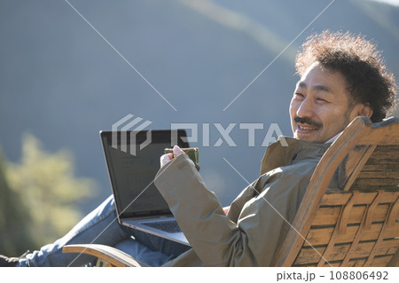 田舎のウッドデッキでリモートワークをする男性の秋冬　カメラ目線のクローズアップ 108806492