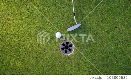 Top view of a golf ball with putter on green course at hole. Top view of a golf ball with putter on green course at hole. 108806683
