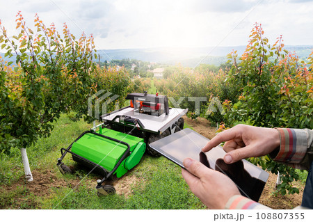 Farmer with digital tablet controls autonomous lawnmower 108807355