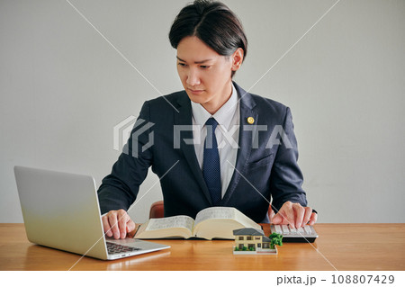 パソコンを見ながら電卓で計算をする男性弁護士 108807429