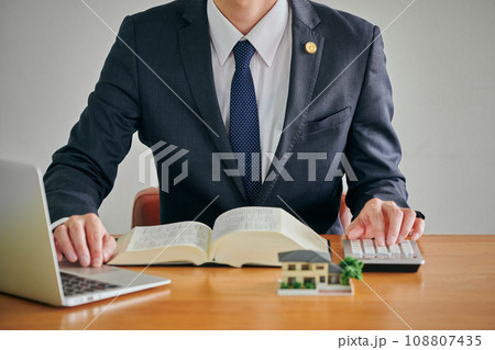 六法全書とパソコンを見ながら電卓で計算をする男性弁護士 108807435