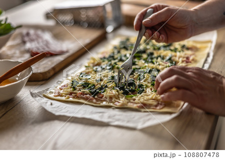 The cook prepares mini pizza cakes, puts spinach on puff pastry with cheese and bacon. 108807478