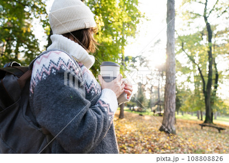 Woman traveler with backpack is holding a cup of hot drink in autumn park 108808826