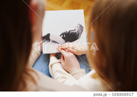 mother and daughter flips through a book with photos of dad and pregnant mom. 108808917