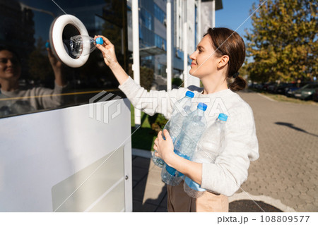Woman uses a self service machine to receive used plastic bottles and cans on a city street 108809577