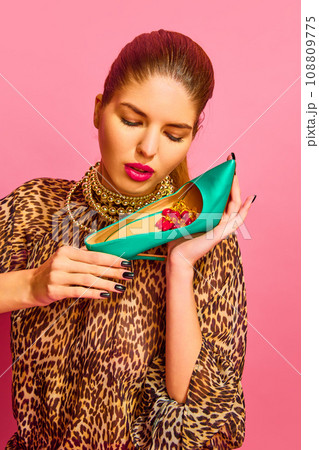 Portrait of lady dressed animal print blouse holding heel full of capsules, vitamins, pills, medications over pink background 108809775