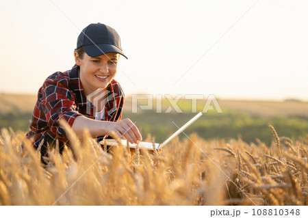 Woman farmer working with laptop on wheat field. 108810348
