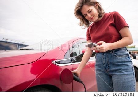 Woman charging red electric car. 108810381