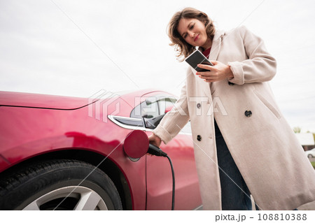 Woman charging red electric car. Woman charging red electric car. 108810388