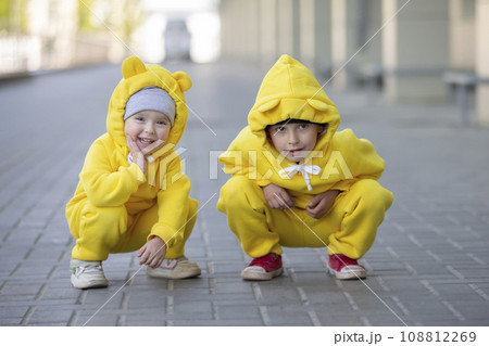Little brother and sister. Funny children boy and girl in yellow identical suits play outdoors. 108812269