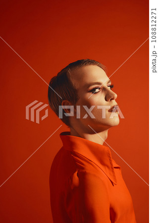 Portrait of young guy in bright jacket, makeup with colorful eyes and lashes posing against red studio background Portrait of young guy in bright jacket, makeup with colorful eyes and lashes posing against red studio background 108812271