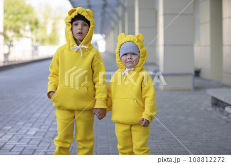 Little brother and sister. Funny kids boy and girl in yellow suits posing, looking at the camera. 108812272