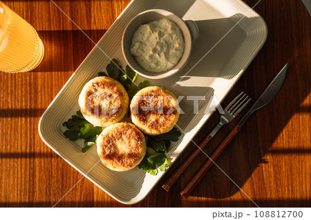 Cheesecakes with sauce with cold drink on a wooden table under sunlight Cheesecakes with sauce with cold drink on a wooden table under sunlight 108812700