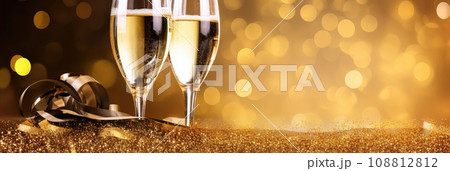 Glasses of champagne on a festive gold bokeh background. New Year or Christmas sparkling horizontal background with copy space. Gold and black colors. 108812812
