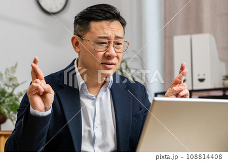 Asian businessman crossed fingers looking at laptop screen asking for good luck news win victory Asian businessman crossed fingers looking at laptop screen asking for good luck news win victory 108814408