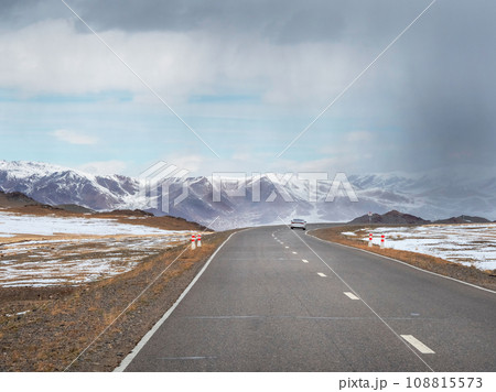 Mongolian snow straight winter road through the hills. Mountain road on a cloudy winter day. Mongolian snow straight winter road through the hills. Mountain road on a cloudy winter day. 108815573