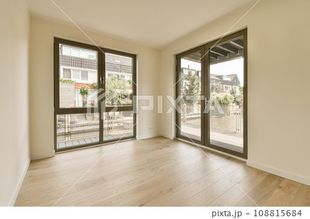 an empty room with wood flooring and sliding glass doors looking out onto the street in front of the house an empty room with wood flooring and sliding glass doors looking out onto the street in front of the house 108815684