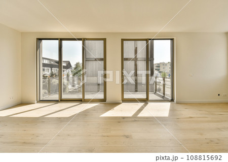 an empty living room with sliding glass doors and hardwood flooring in the middle part of the room is white an empty living room with sliding glass doors and hardwood flooring in the middle part of the room is white 108815692