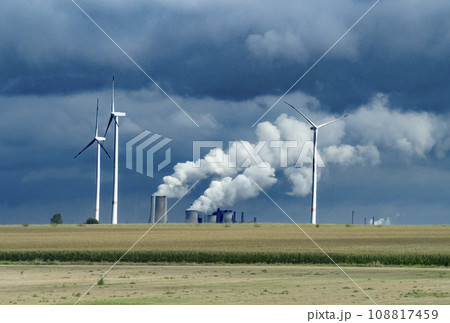 Wind turbines and industrial pipes with smoke on a cloudy day in Germany 108817459