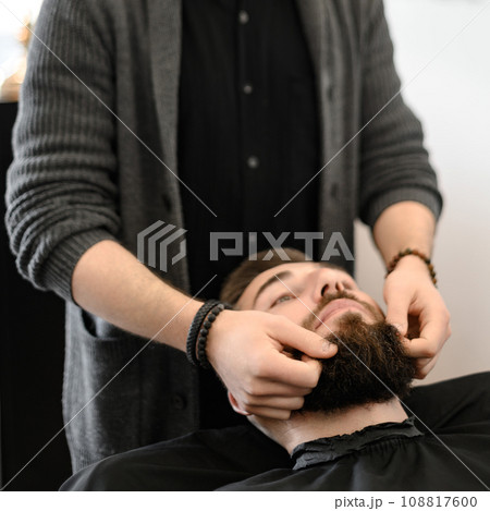 A barber massages and rubs a male client beard after applying moisturizing oil A barber massages and rubs a male client beard after applying moisturizing oil 108817600