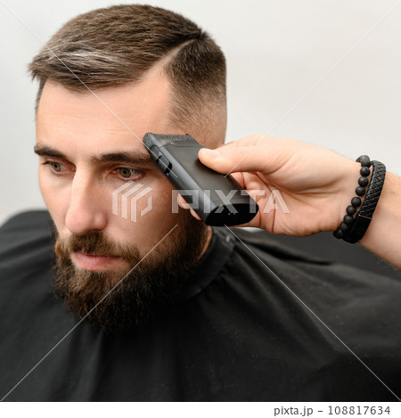 Barber shaves the temple with cordless trimmer during a short haircut on the sides of the head. 108817634