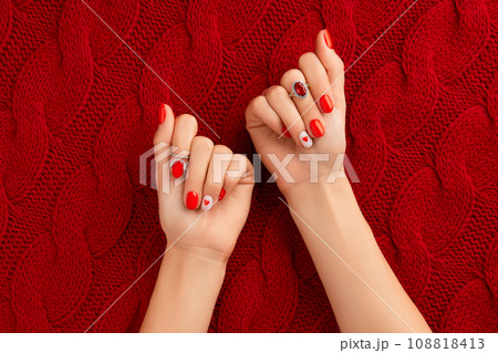 Manicured womans hands on knitted wool red fabric. Fashionable valentines day nail design Manicured womans hands on knitted wool red fabric. Fashionable valentines day nail design 108818413