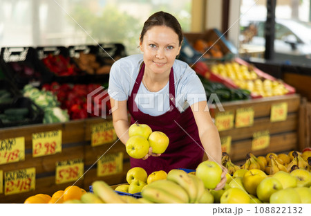 Woman seller working in supermarket and lays out apples on counter 108822132