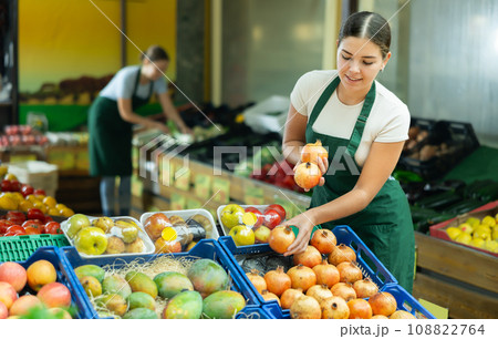 Smiling salesgirl arranging pomegranates on counter at farmers market Smiling salesgirl arranging pomegranates on counter at farmers market 108822764