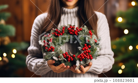 A woman holds a festive Christmas composition, a bouquet of fir branches with red berries and holly branches 108823601