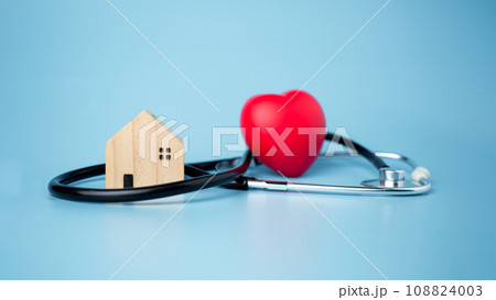Concept of health insurance and medical welfare, small wooden house and red heart with stethoscope on blue background, health insurance and access to healthcare. Concept of health insurance and medical welfare, small wooden house and red heart with stethoscope on blue background, health insurance and access to healthcare. 108824003
