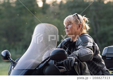 Blonde motorcycle tourist, wearing black gloves, sitting on her bike, begins to move carefully. 108827313