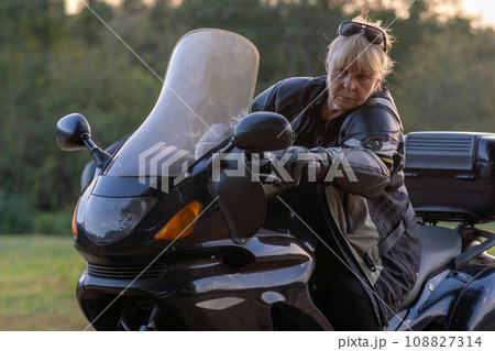 Pretty middle-aged female motorcyclist in leather jacket and black gloves on autumn day. Hobby . 108827314