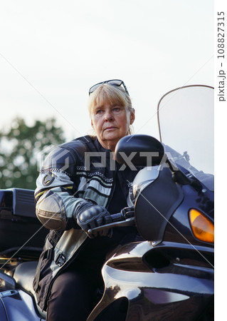 Beautiful vertical portrait of pretty female motorcyclist sitting on her motorcycle on autumn day. 108827315