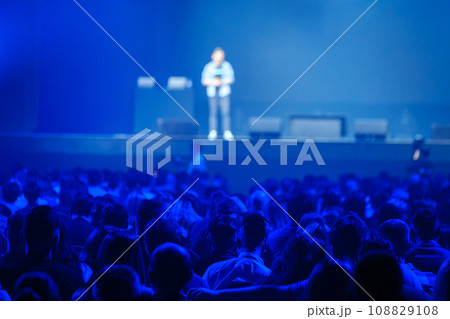 Back view of businesspeople watching speaker on stage in blue illuminated stadium 108829108