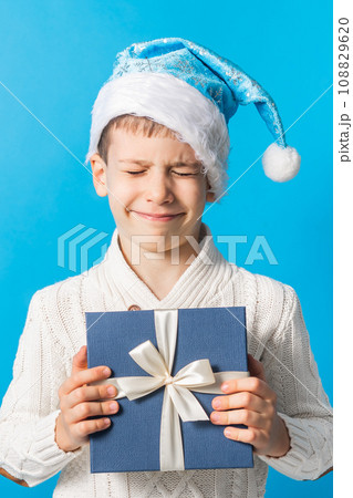 Child boy gift. Kid in blue christmas hat holds gift box. Shopping time, copy space and empty space for text. Generation alpha and gen alpha Child boy gift. Kid in blue christmas hat holds gift box. Shopping time, copy space and empty space for text. Generation alpha and gen alpha 108829620