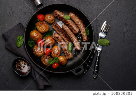 Delicious grilled sausages and potatoes in a sizzling frying pan Delicious grilled sausages and potatoes in a sizzling frying pan 108830803