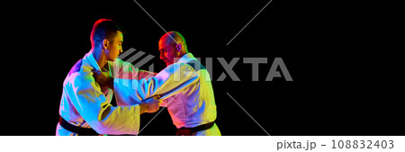 Banner. Portrait of two man looking eyes to eye while fighting in neon light isolated black background with negative space to insert your text. 108832403