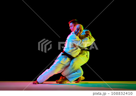 Two young professional karate men fighting, performing technical skill in neon light isolated black background. Copy space for ad, text Two young professional karate men fighting, performing technical skill in neon light isolated black background. Copy space for ad, text 108832410