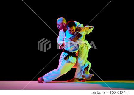 Two male professional sportsmen during match. Karate fighter attacking his opponent with leg technique isolated black background. 108832413
