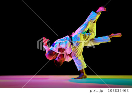 Portrait of two athletic, strong men, professional judokas, fighters showing their skills in neon light while competition isolated black background. 108832468