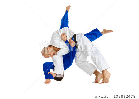 Portrait of two male sportsmen, martial arts fighters in white and blue kimono fighting performing techniques in motions isolated white background. Portrait of two male sportsmen, martial arts fighters in white and blue kimono fighting performing techniques in motions isolated white background. 108832478