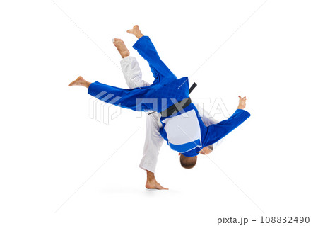 Two male professional sportsmen during match. Judo fighter attacking his opponent with leg technique isolated white background. Two male professional sportsmen during match. Judo fighter attacking his opponent with leg technique isolated white background. 108832490