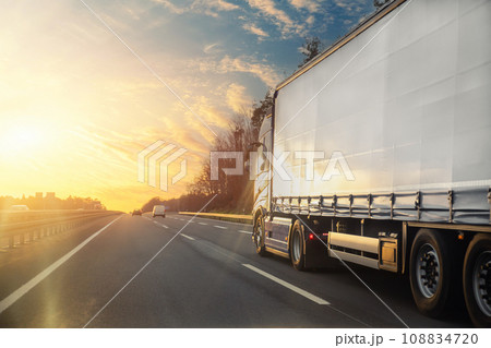 Tail view white blank modern delivery big shipment cargo commercial semi trailer truck moving motorway road city urban suburb. Business distribution logistics service. Lorry driving highway sunset 108834720